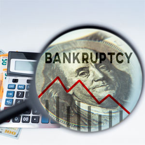Magnifying glass highlighting bankruptcy on a dollar bill with a declining graph.